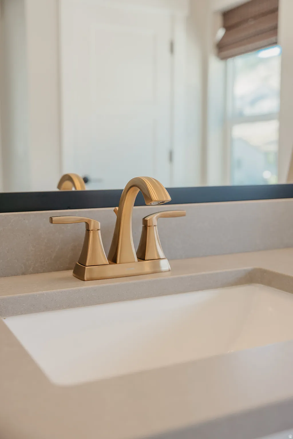 Integrated vanity sink with a gold-finish faucet, featuring a light gray countertop and a framed mirror