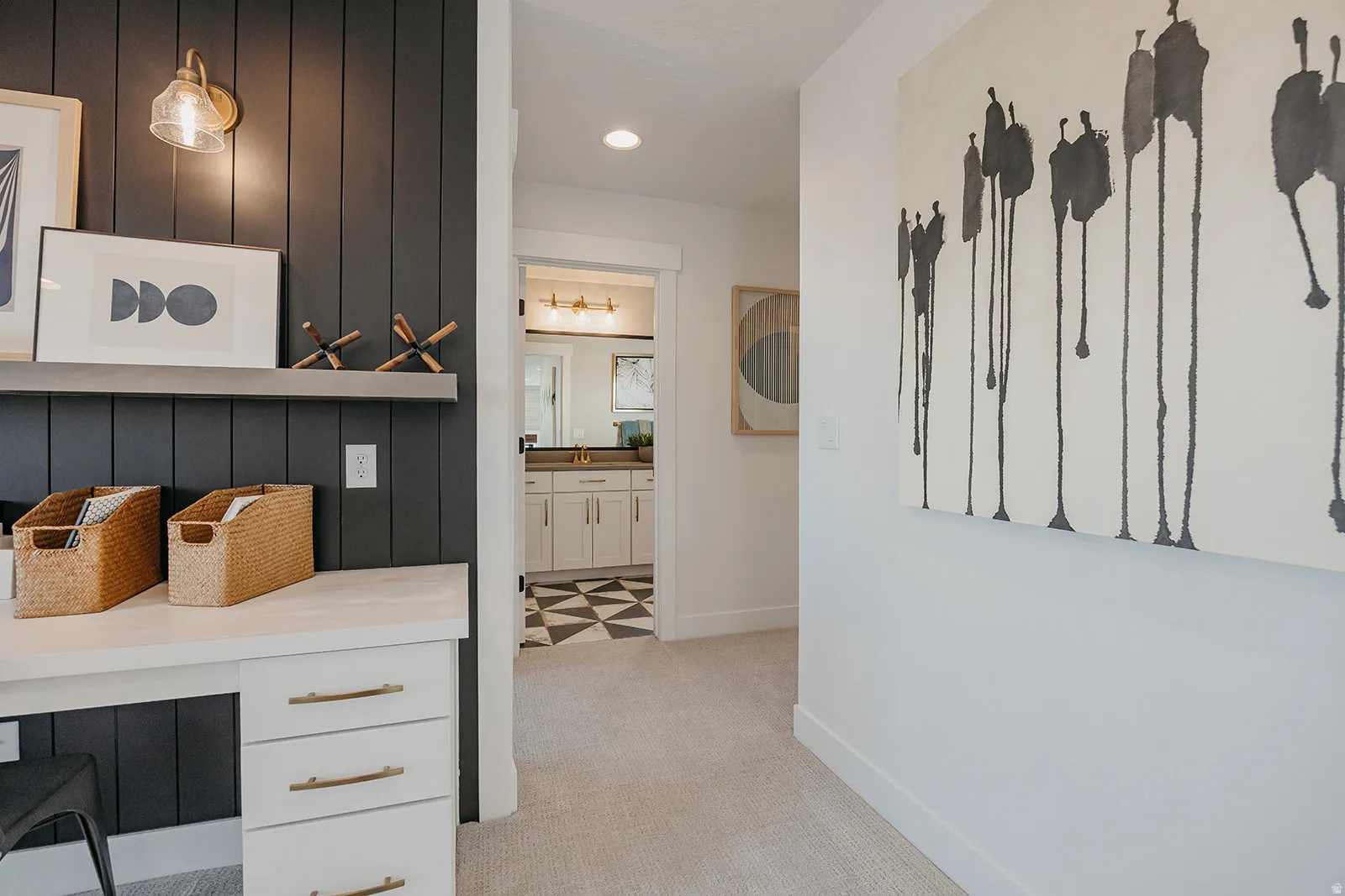 Built-in white desk with brass drawer pulls, dark vertical paneling, and an overhead wall sconce
