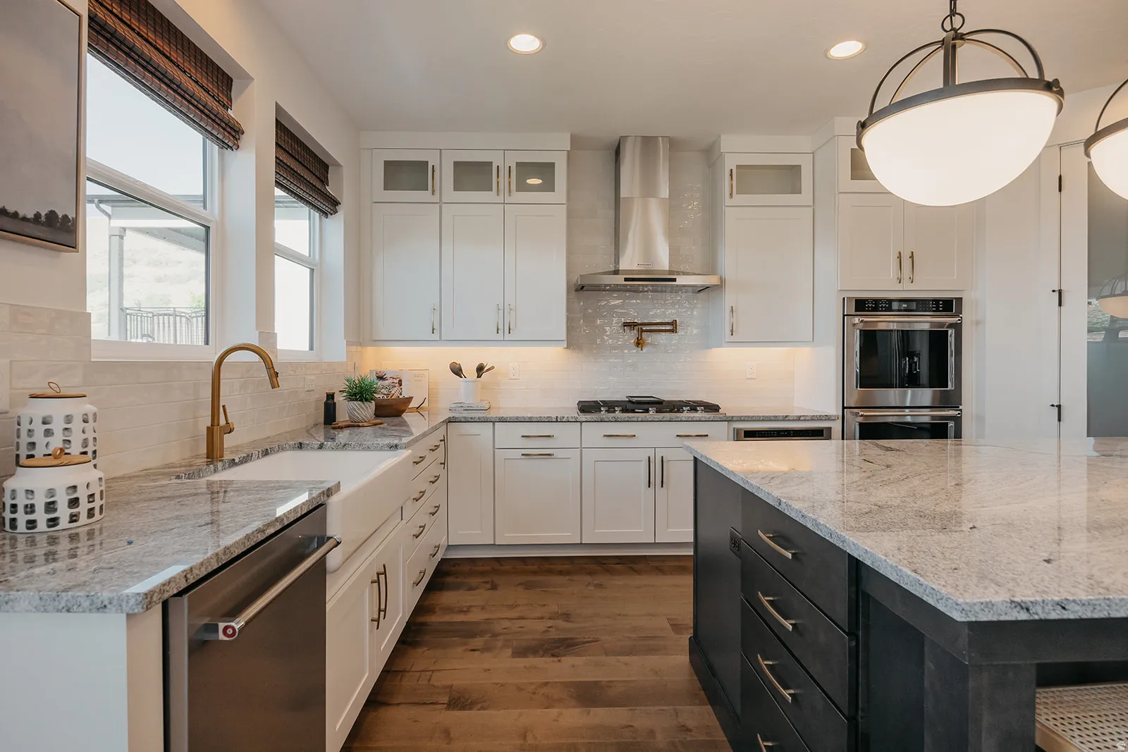 Gourmet kitchen featuring a large island, white shaker cabinetry, stainless steel appliances, a farmhouse sink with a brass faucet, and wood-finish flooring