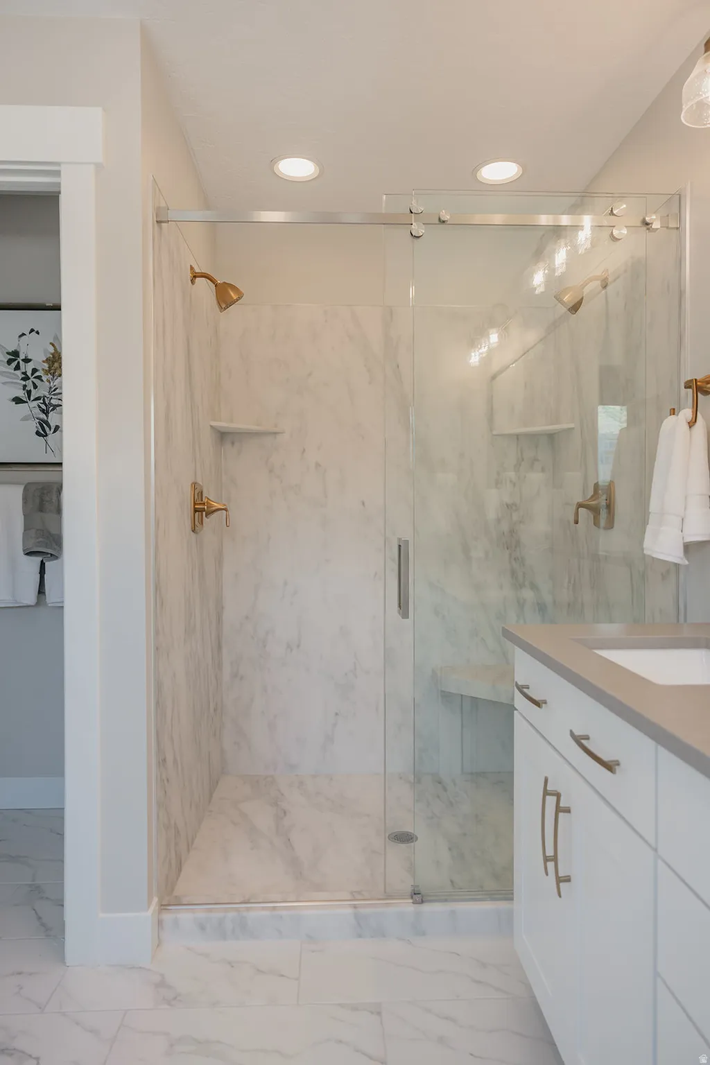 Spacious shower enclosure with marble-look tile, clear glass sliding doors, and dual gold-toned shower fixtures