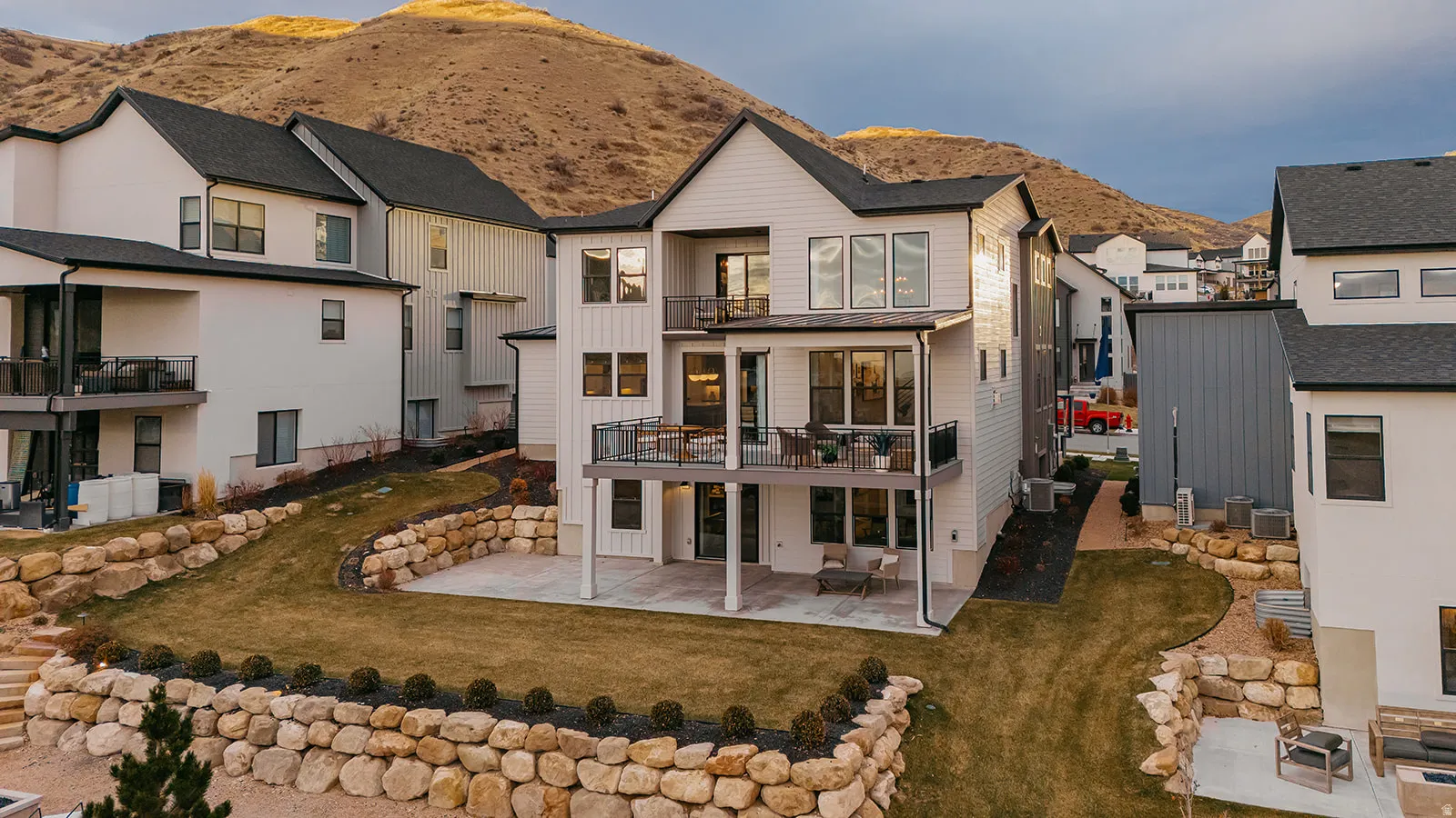 Modern multi-story residence with white siding and black trim, featuring a tiered backyard with stone retaining walls