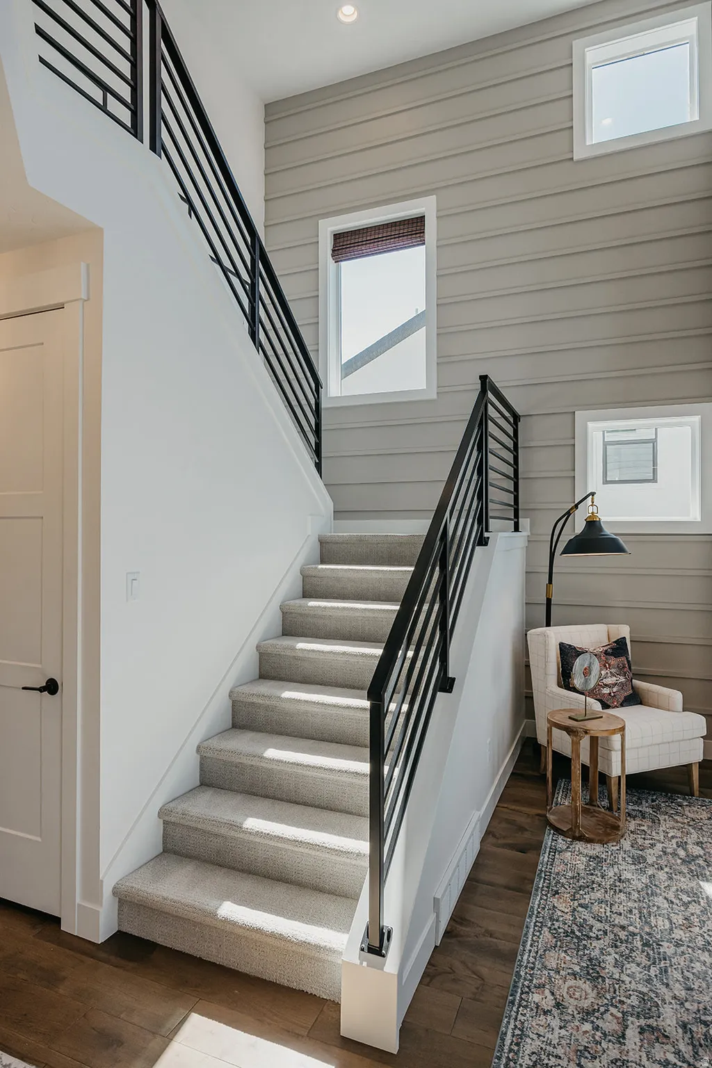Carpeted staircase with contemporary black metal railings, complemented by hardwood-finish flooring