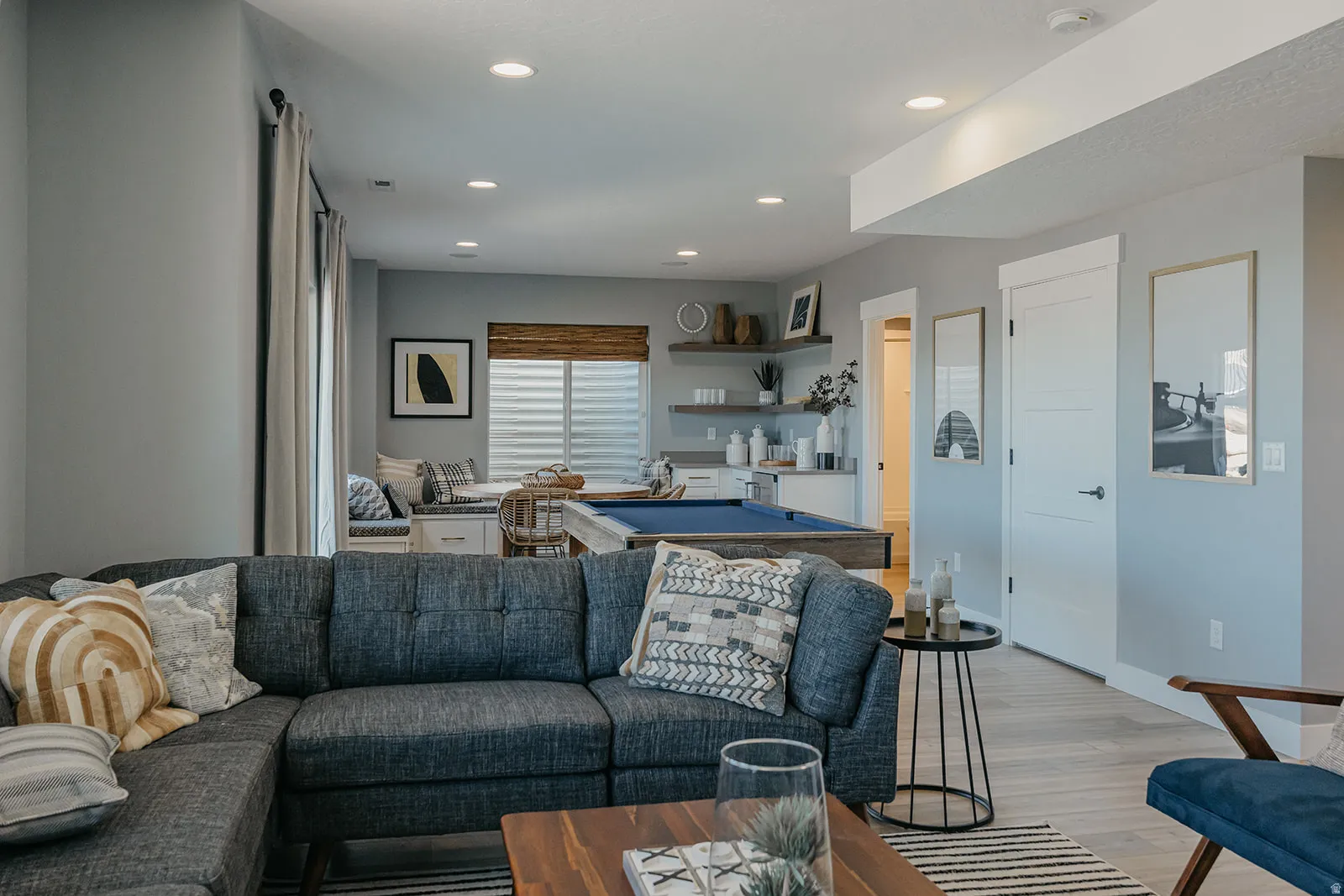 Open-concept lower level featuring recessed lighting, light wood-finish flooring, and a built-in wet bar with floating shelves