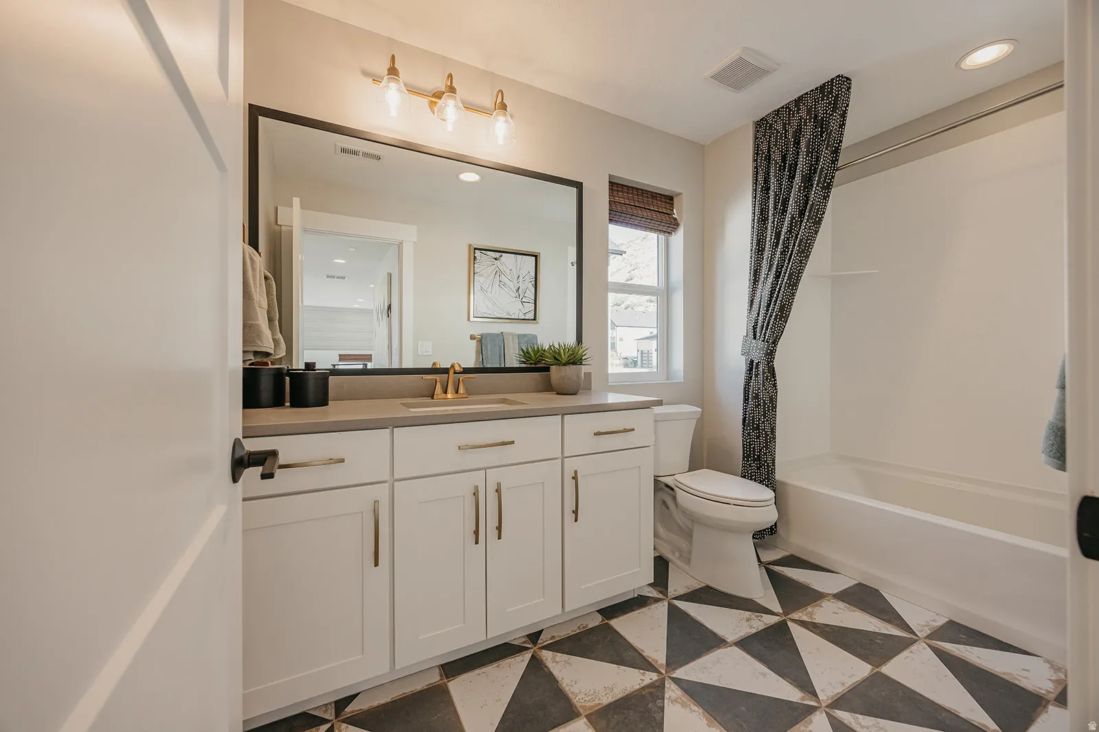 Contemporary bathroom featuring a patterned floor, white shaker cabinetry with gold-finish hardware, a full-width mirror, and a gold-finish vanity faucet