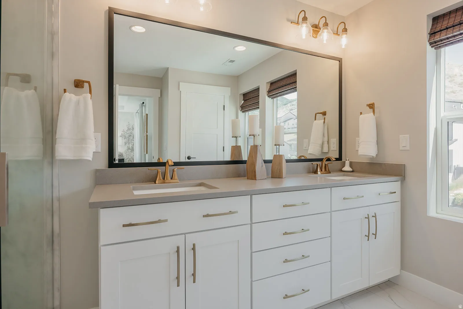Double vanity featuring white shaker-style cabinetry with gold-tone hardware, a light-toned countertop, and dual integrated sinks