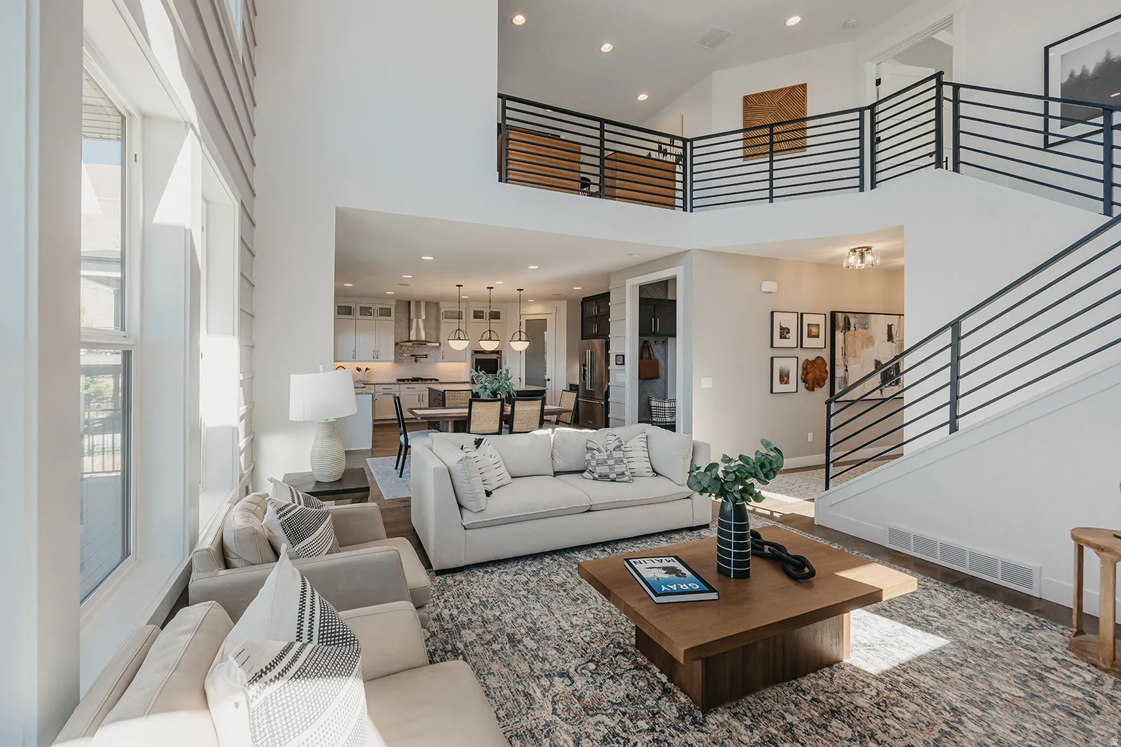 Two-story living room featuring a double-height ceiling, large windows, a two-story staircase with contemporary metal railings, and wood-finish flooring
