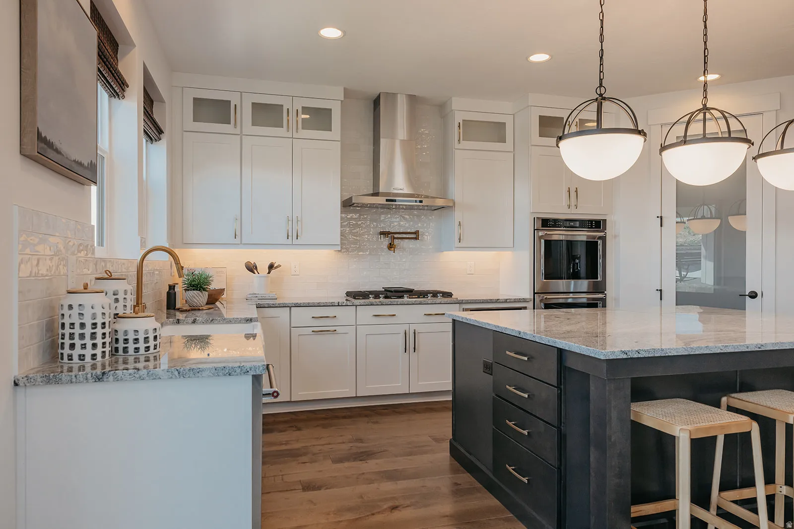 Spacious kitchen featuring an expansive center island with seating, granite countertops, wood-finish flooring, white cabinetry with glass-front accents, and stainless steel appliances
