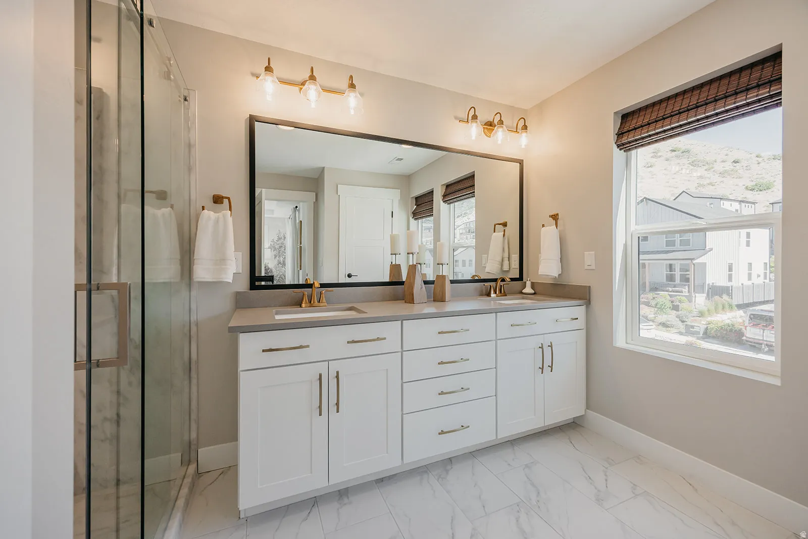 Dual vanity featuring white shaker cabinetry, gold-tone fixtures, and a large framed mirror