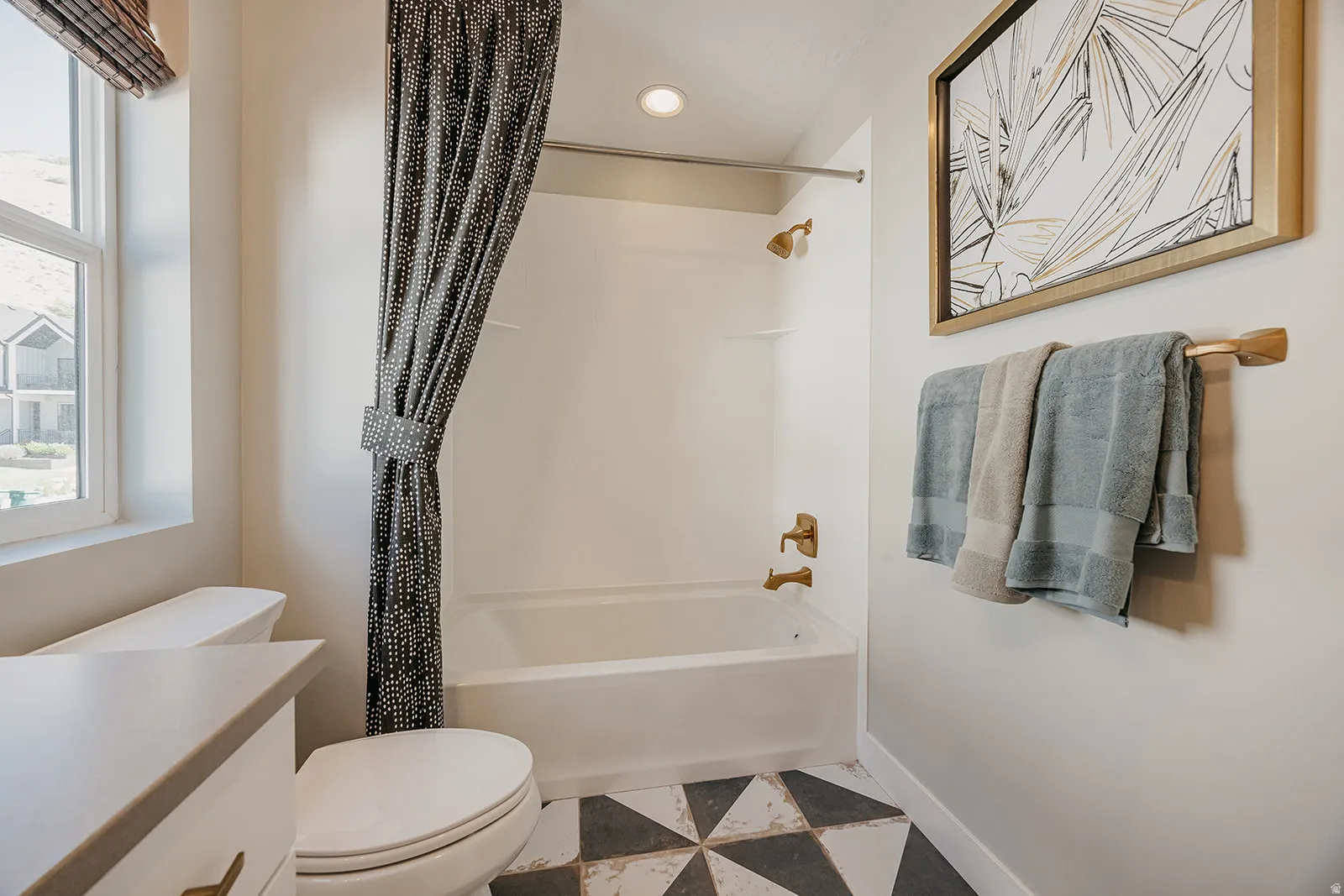 Bathroom featuring a built-in tub and shower combination with bronze-finish fixtures, a single window, and a patterned tile floor