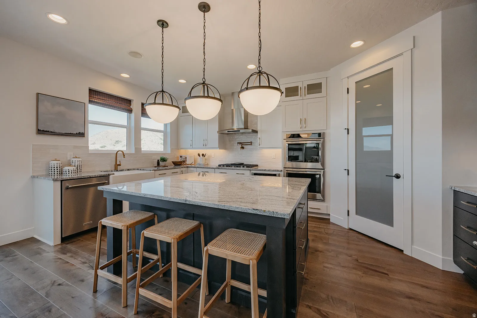 Spacious kitchen featuring a large island with a stone countertop, wood-finish flooring, recessed lighting, and stainless steel appliances, including double ovens