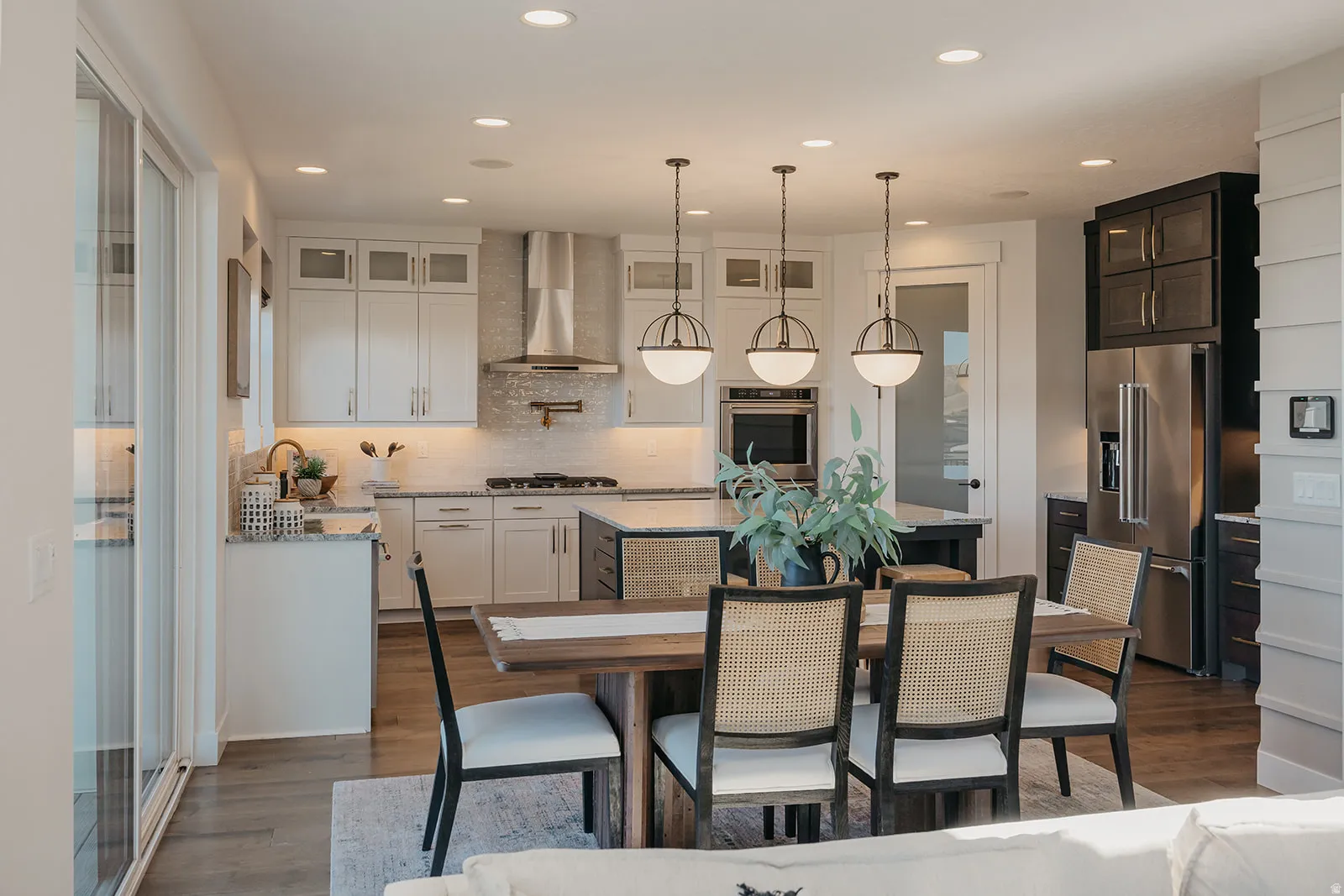 Open-concept kitchen and dining area featuring a kitchen island with an integrated sink, stainless steel appliances, white cabinetry with glass inserts, and wood-finish flooring