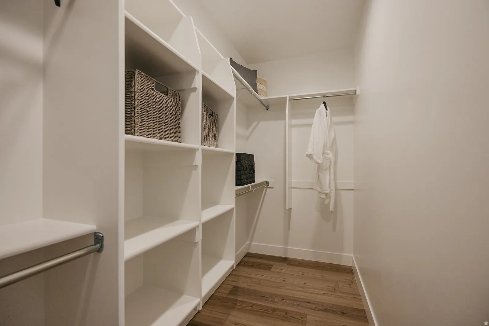 Walk-in closet featuring extensive built-in shelving, multiple hanging rods, white walls, and wood-finish flooring