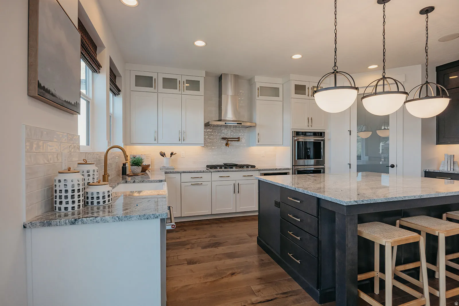 Gourmet kitchen with a large island featuring bar seating, stainless steel appliances including a built-in oven and microwave, white shaker cabinetry, and wood-finish flooring