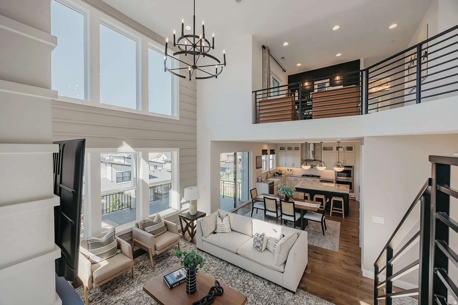 Two-story living area with high ceilings, featuring a contemporary chandelier, shiplap accent wall, and wood-finish flooring