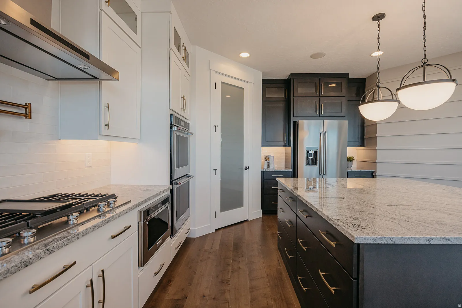 Contemporary kitchen featuring white perimeter cabinetry, a dark-toned island, stainless steel appliances, granite countertops, and wood-finish flooring