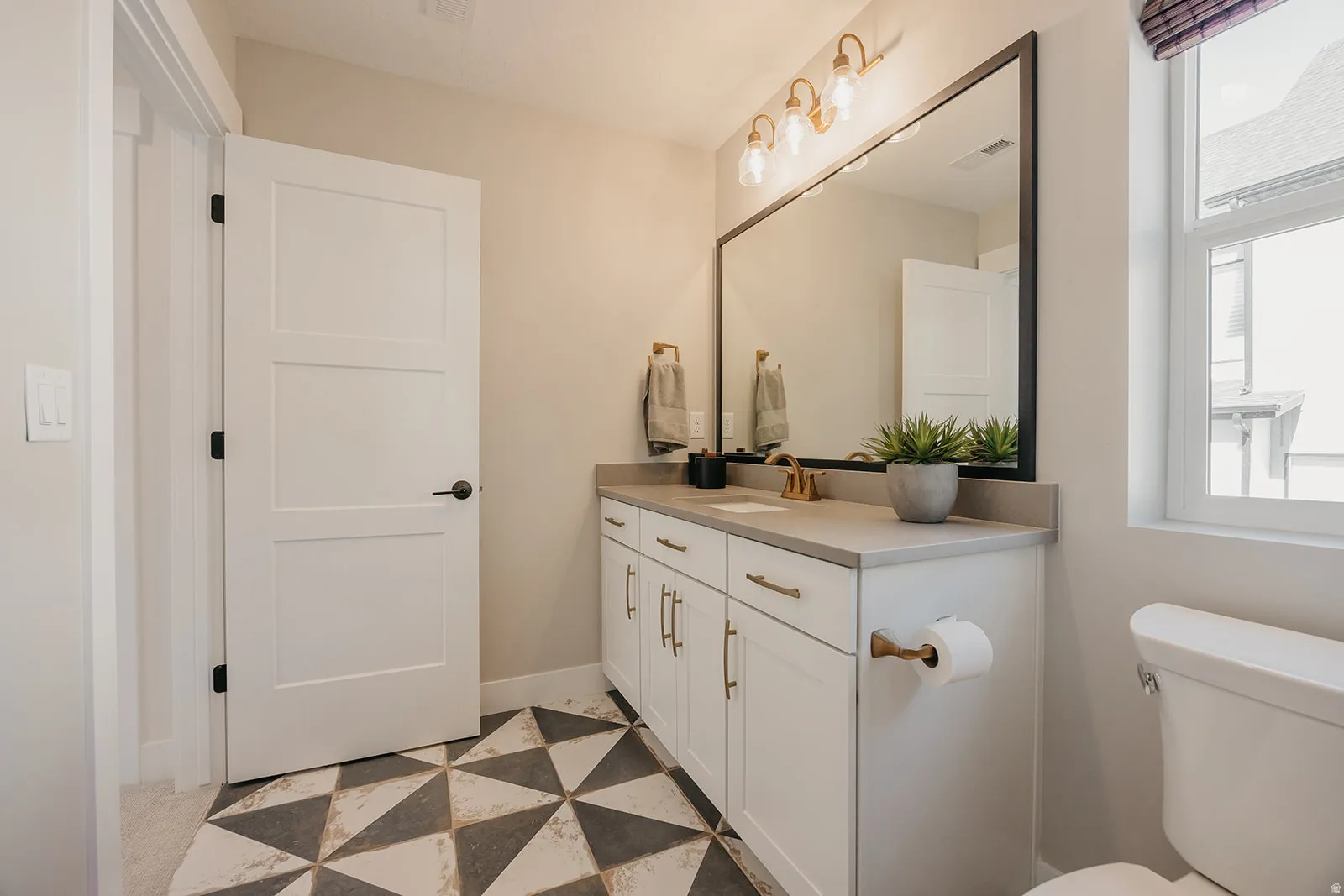 Bathroom featuring a white vanity with gold-tone hardware, a light-toned countertop, and a large framed mirror
