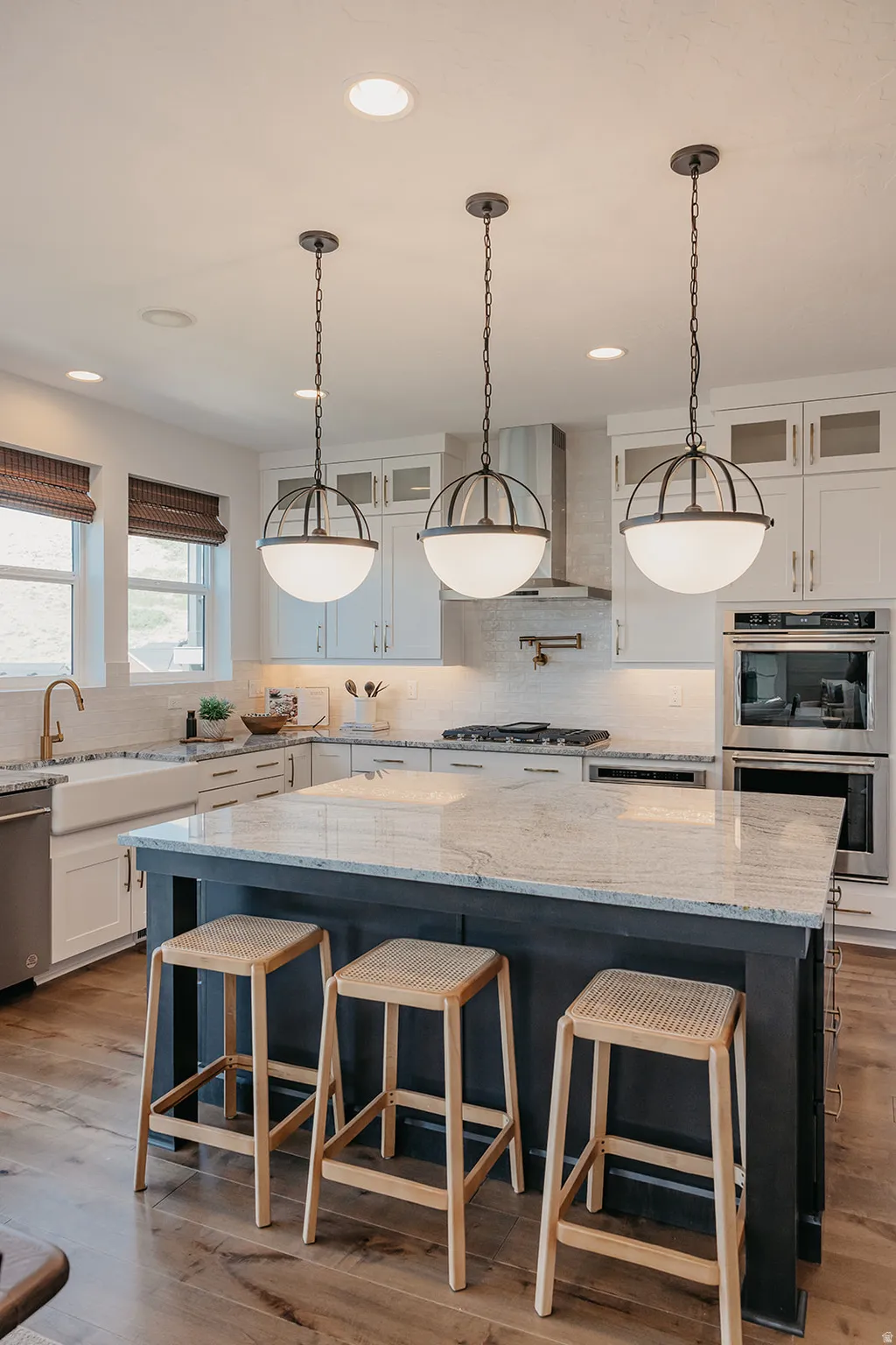 Kitchen featuring a large island with a light-toned countertop, three pendant lights, wood-finish flooring, white cabinetry, and stainless steel appliances