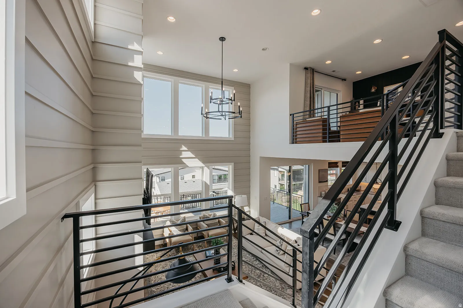 Multi-level interior featuring a contemporary chandelier, large windows providing ample natural illumination, a second-story landing with an open railing, a staircase with carpeted treads, and modern metal balusters