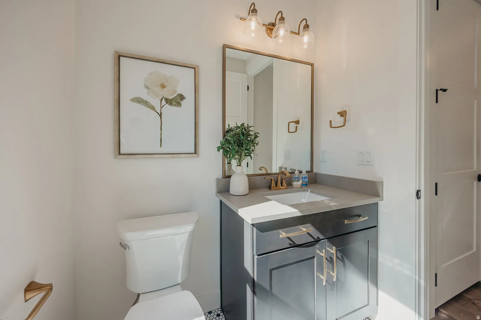 Vanity featuring dark cabinetry with gold hardware, a rectangular undermount sink, and a light-toned countertop