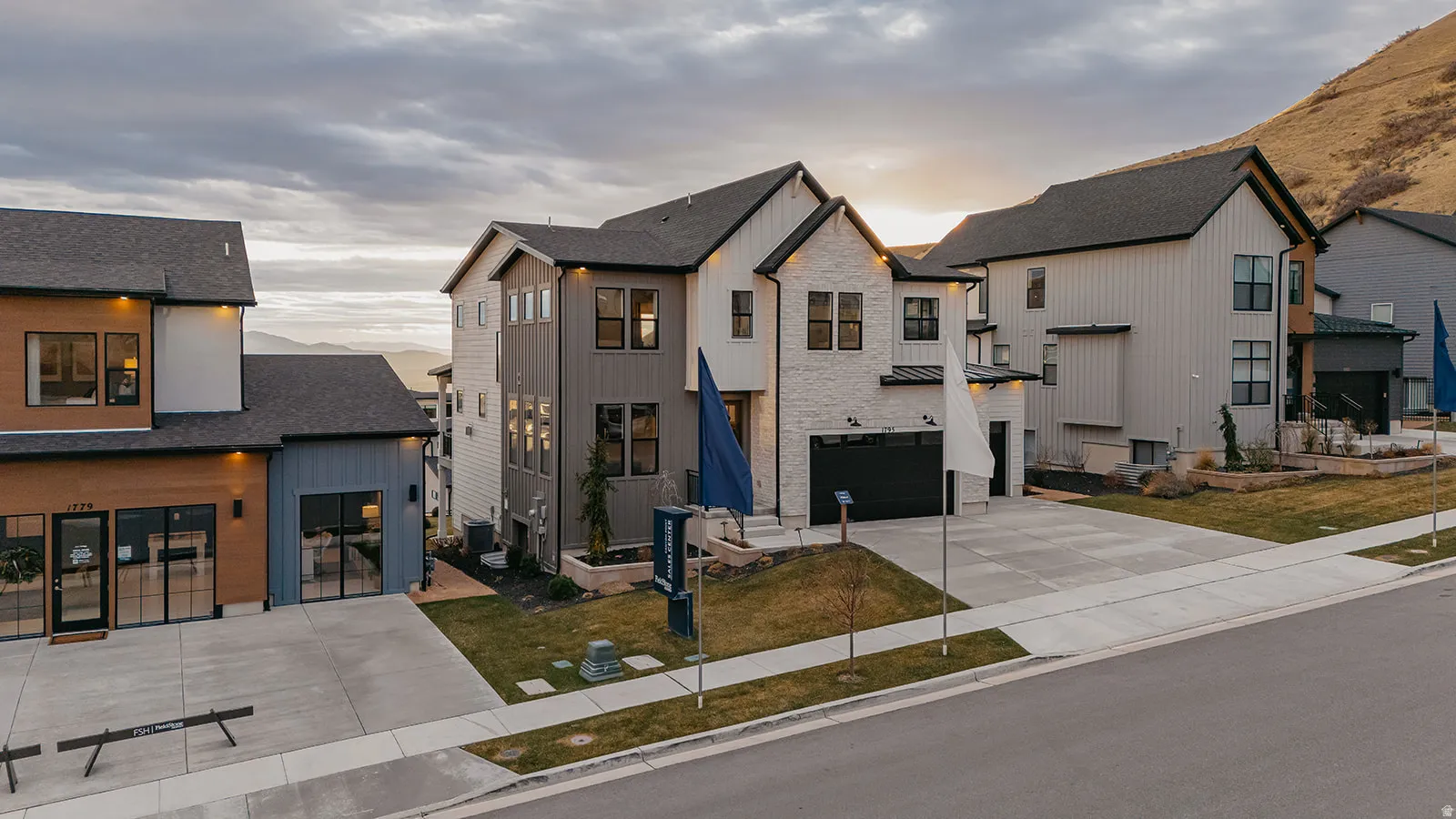 Modern multi-level exterior featuring a two-car garage, dark-framed windows, a blend of white brick and dark vertical siding, and a sloped roofline