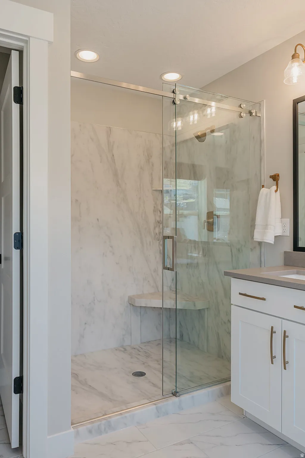 Walk-in shower featuring a frameless glass enclosure, built-in bench, marble-finish wall panels, and recessed lighting