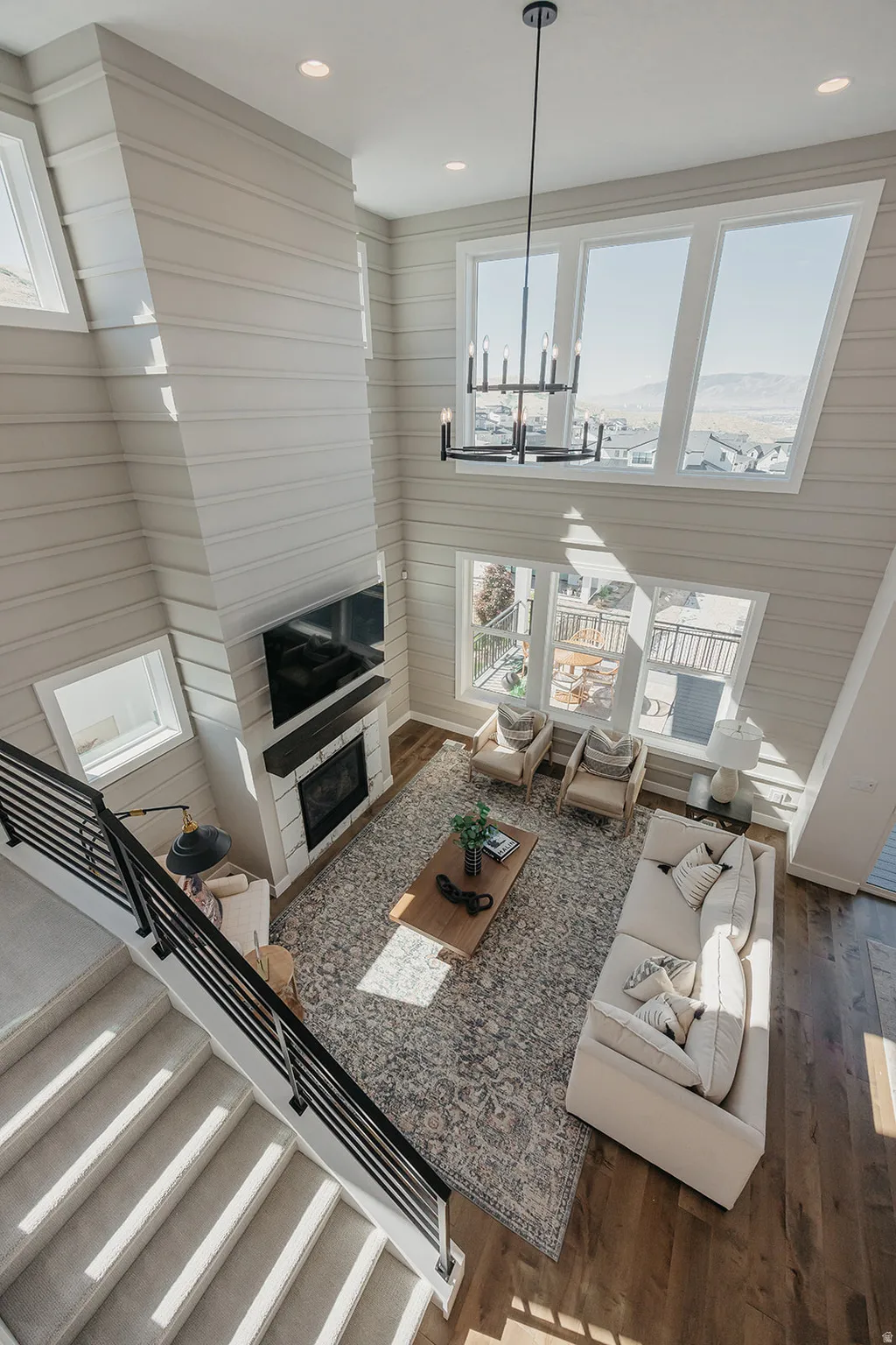Two-story living area featuring a prominent fireplace, high ceilings, large windows, wood-finish flooring, and a modern chandelier