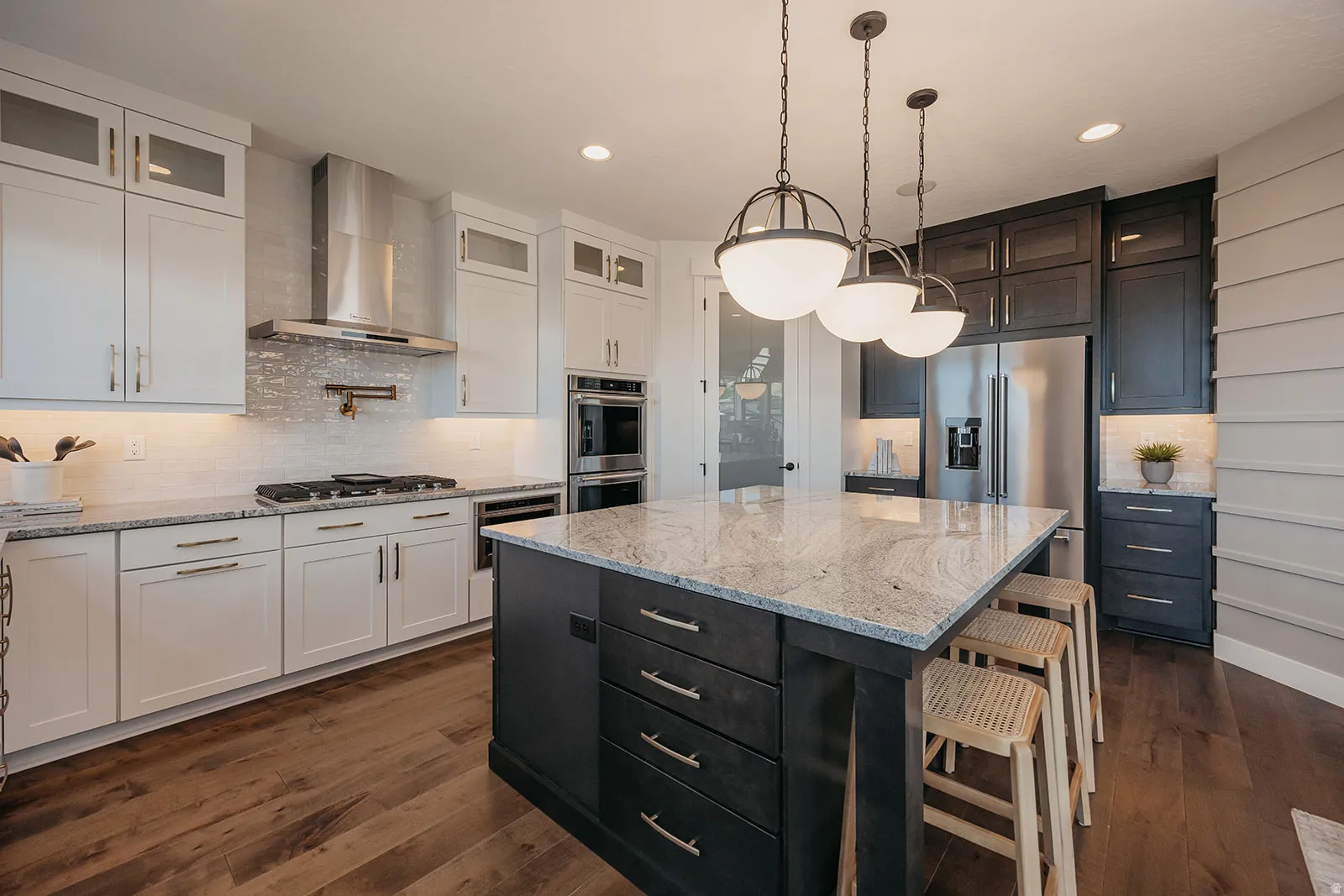 Gourmet kitchen featuring a large central island with seating, stainless steel appliances, white and dark cabinetry, wood-finish flooring, and pendant lighting