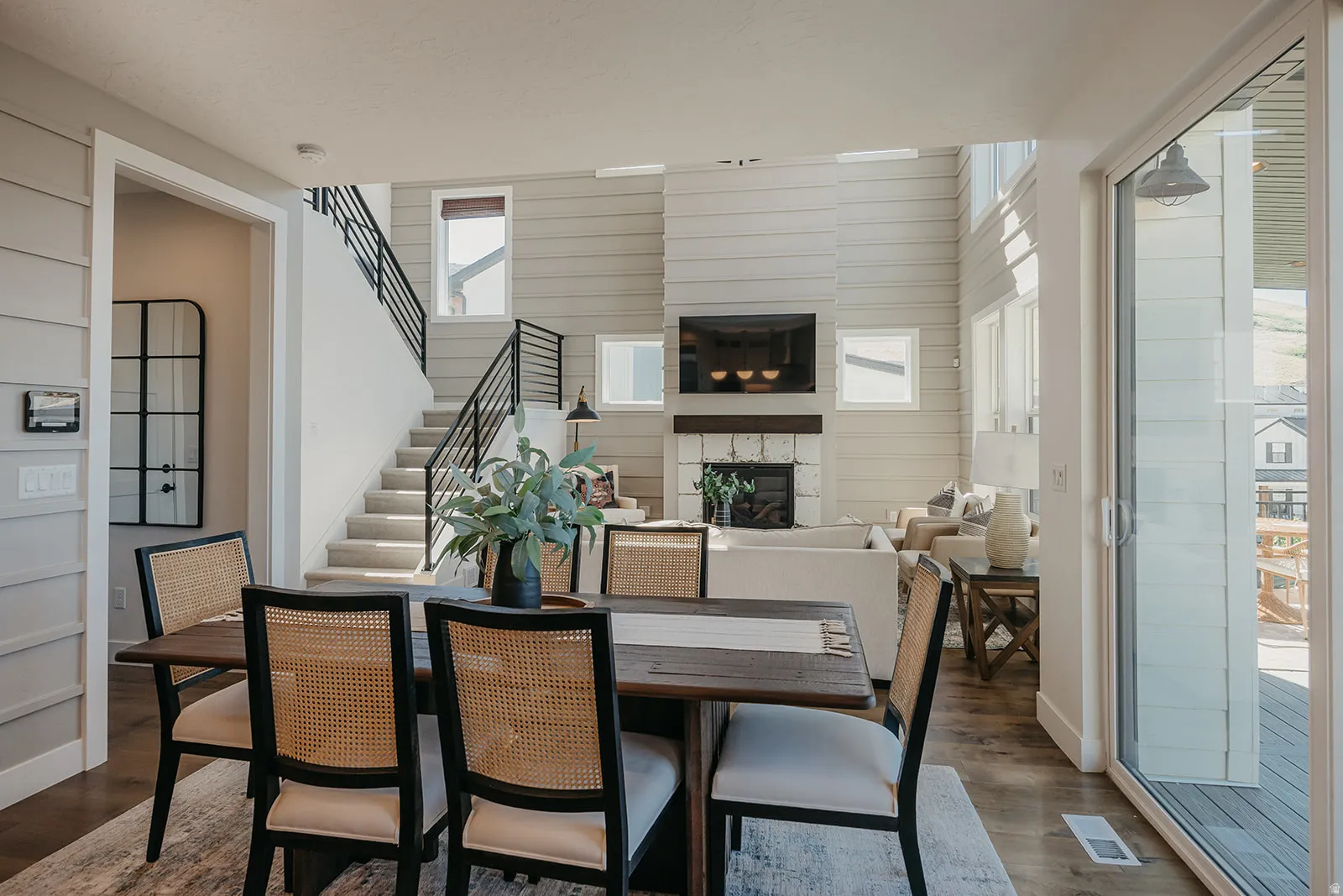 Open-concept living area featuring a dining space with wood-finish flooring, a two-story shiplap accent wall, and a fireplace with a stone surround