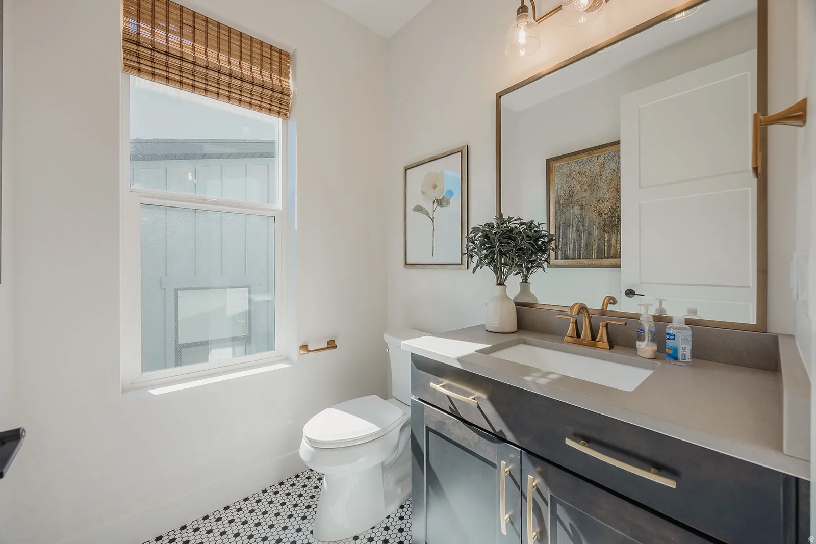 Bathroom featuring a single vanity with dark cabinetry, brass hardware, and a light-toned countertop