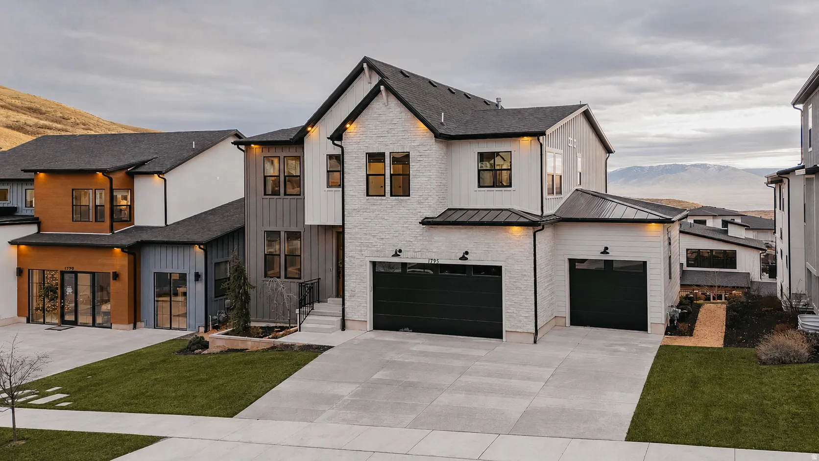 Modern exterior featuring a prominent two-car garage, white stone facade, and dark framed windows