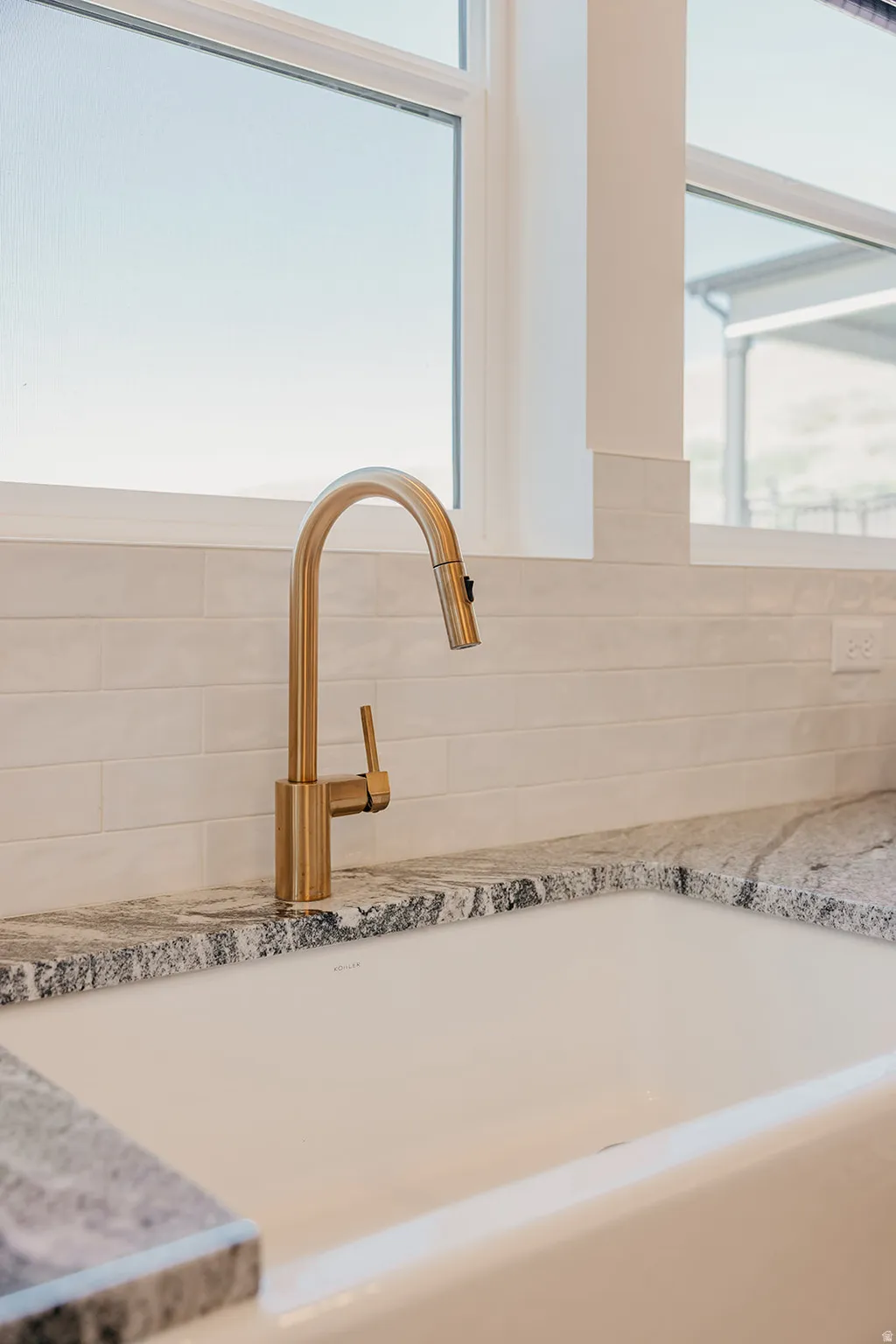 Farmhouse sink with a gold-tone gooseneck faucet, set against a white subway tile backsplash and variegated stone countertops