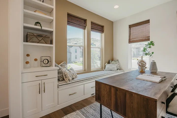 Integrated window seat with built-in storage drawers, bordered by multiple windows with woven Roman shades