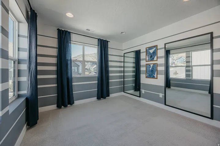 Spacious room featuring light-colored carpeting, horizontal striped wall accents, and multiple windows providing natural illumination