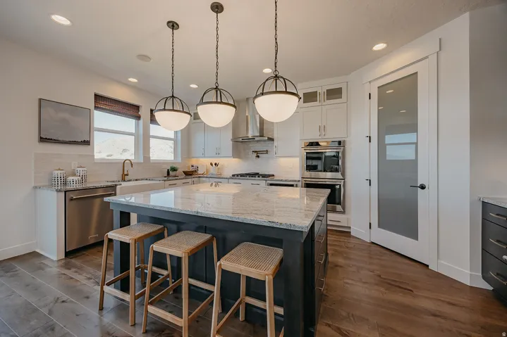 Spacious kitchen featuring a large island with a stone countertop, wood-finish flooring, recessed lighting, and stainless steel appliances, including double ovens