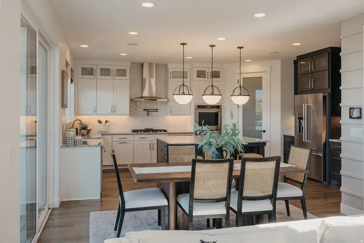 Open-concept kitchen and dining area featuring a kitchen island with an integrated sink, stainless steel appliances, white cabinetry with glass inserts, and wood-finish flooring