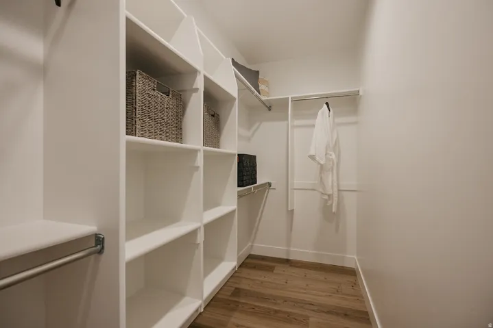 Walk-in closet featuring extensive built-in shelving, multiple hanging rods, white walls, and wood-finish flooring