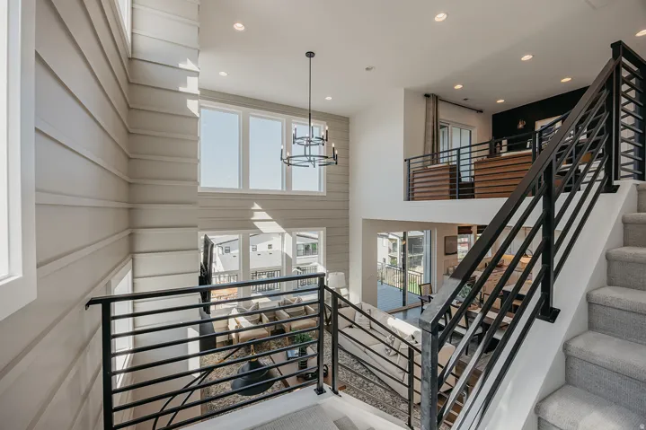 Multi-level interior featuring a contemporary chandelier, large windows providing ample natural illumination, a second-story landing with an open railing, a staircase with carpeted treads, and modern metal balusters