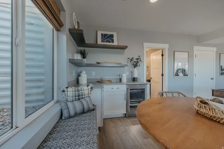 Built-in window bench with patterned upholstery, a wet bar featuring white cabinetry, a beverage refrigerator, and open shelving, all complemented by wood-finish flooring