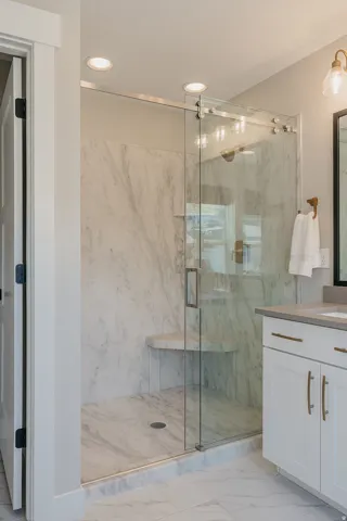 Walk-in shower featuring a frameless glass enclosure, built-in bench, marble-finish wall panels, and recessed lighting