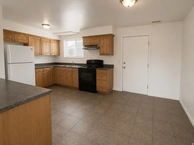 Unit A: Kitchen featuring wood cabinetry, dark countertops, and tile flooring