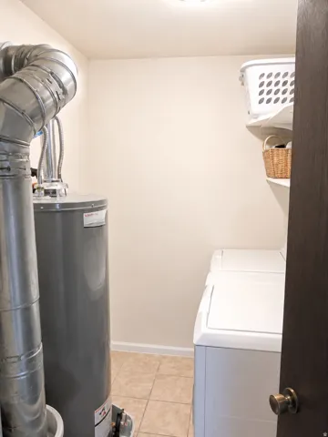 Unit B: Laundry area featuring a water heater with metal ductwork, tile flooring, and built-in shelving