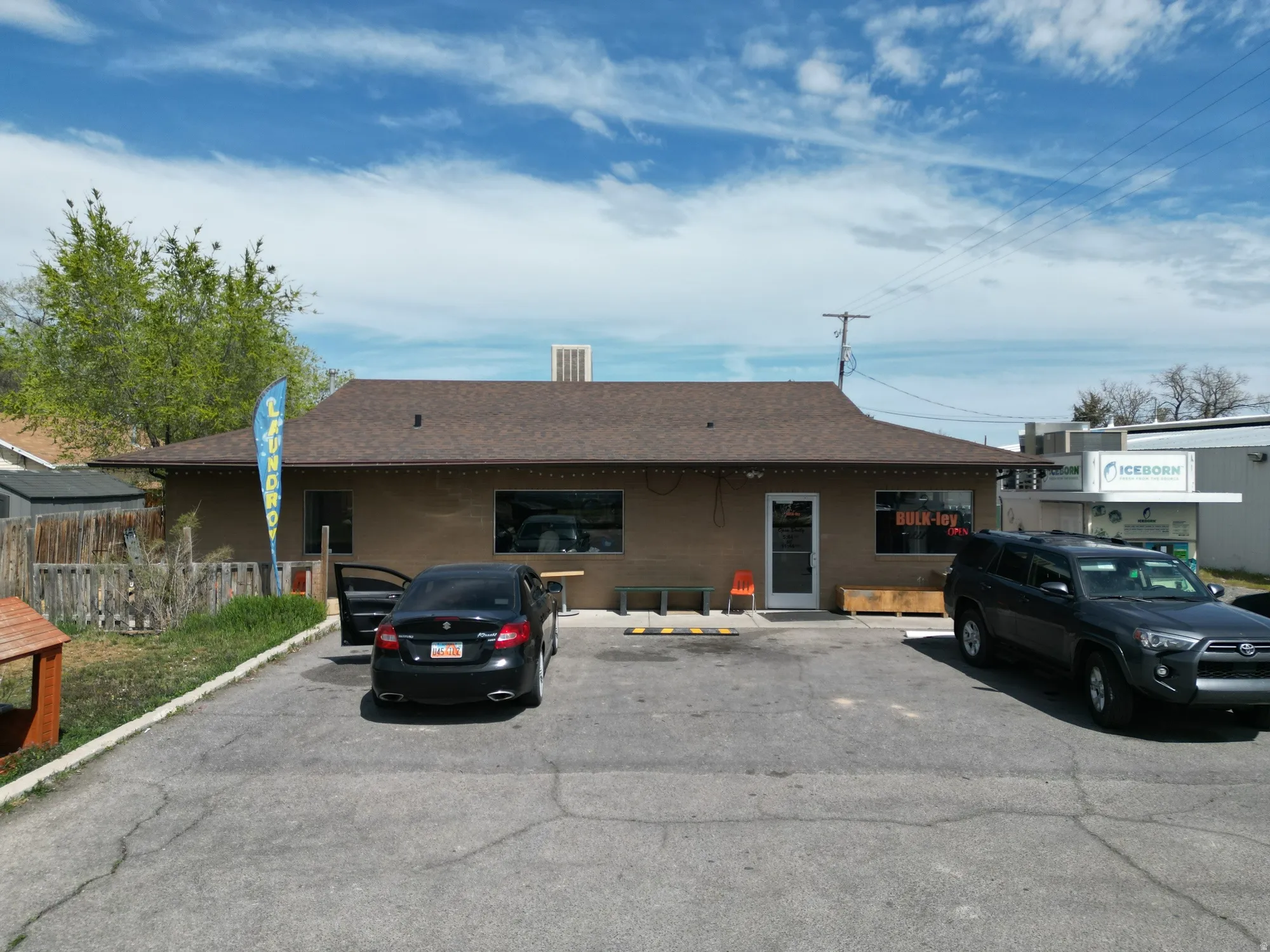 Single-story commercial building with a brown stucco exterior, dark shingle roof, and a prominent storefront entrance