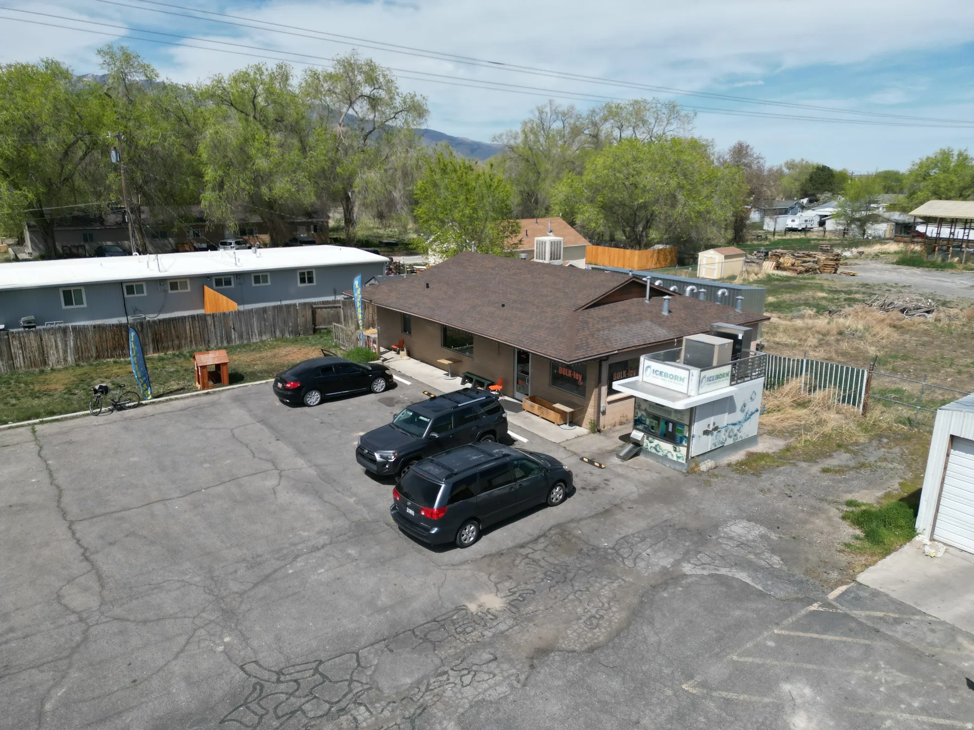 Commercial building featuring a brown shingle roof, an adjacent drive-thru structure, a paved parking area, and an exterior side fence