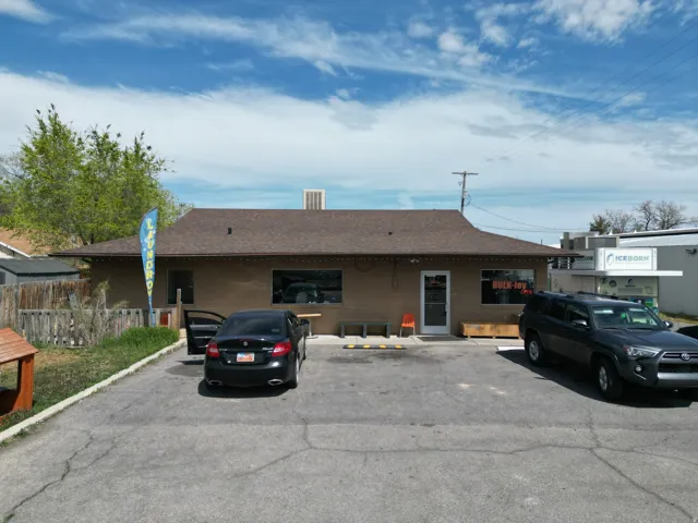 Single-story commercial building with a brown stucco exterior, dark shingle roof, and a prominent storefront entrance