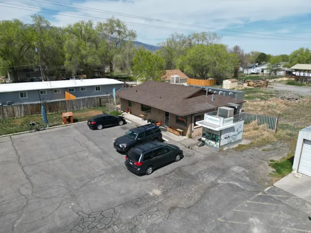 Commercial building featuring a brown shingle roof, an adjacent drive-thru structure, a paved parking area, and an exterior side fence