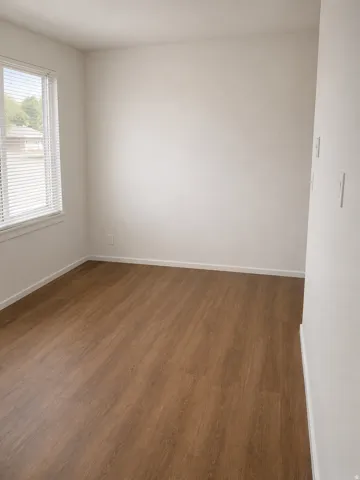 Unit B: Bright interior space featuring wood-finish flooring, white baseboards, and a window with blinds