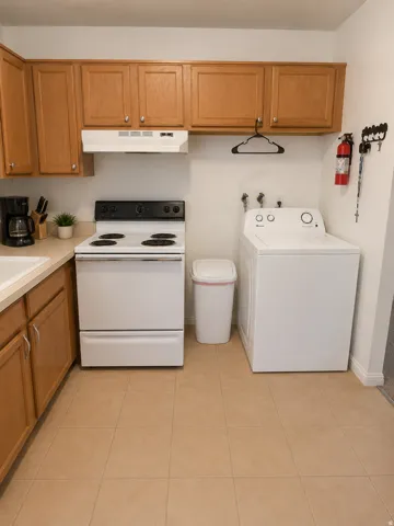 Unit D: Kitchen area featuring wood-finish cabinetry, a white electric range with a range hood, and a white top-load washing machine