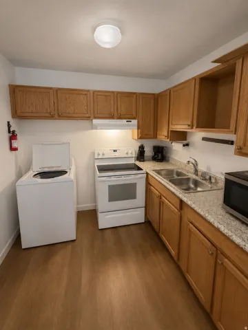 Unit B: Kitchen featuring wood-finish flooring, light wood cabinetry, stone-look countertops, and a double basin stainless steel sink