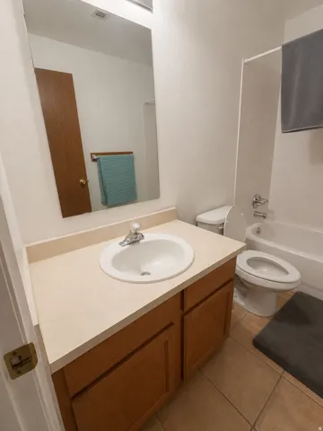 Unit D: Bathroom featuring a wood-finish vanity with a laminate countertop, an integrated sink with chrome fixtures, a full-width mirror, and a white bathtub with a shower