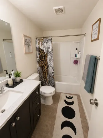 Unit C: Bathroom featuring a dark wood-finish vanity with a white solid surface countertop, an integrated sink, and brushed nickel hardware